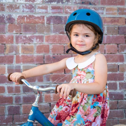 Child wearing a blue CoConuts helmet sitting on a blue Trybike in front of a brick wall.