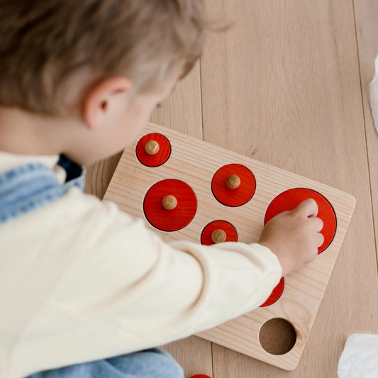 Child playing with a QToys Montessori size sorting wooden puzzle toy on a wooden floor
