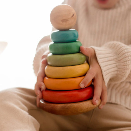 Child holding a colorful QToys wooden stacking toy