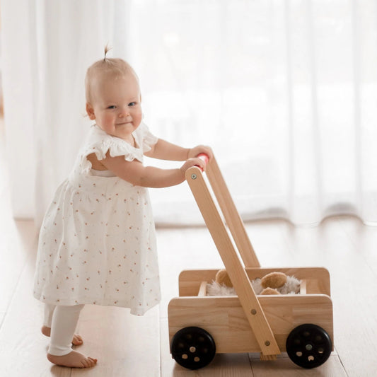 Toddler learning to walk with QToys Classic Wooden Baby Walker Trolley, from Curious Moonbeam