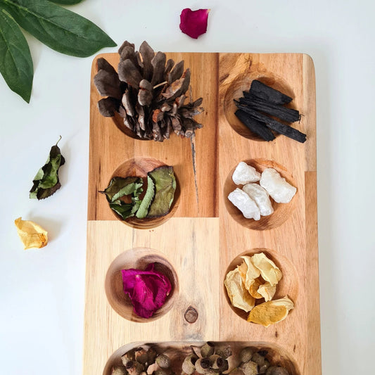 Wooden montessori sorting tray with compartments containing various dried herbs and flowers on a white background.