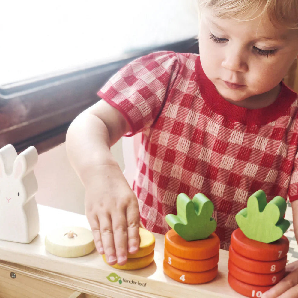 Child playing with Tender Leaf Toys' Counting Carrots wooden numeracy toy on a table.
