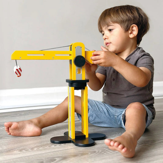 Child playing with a toy crane on a wooden floor.